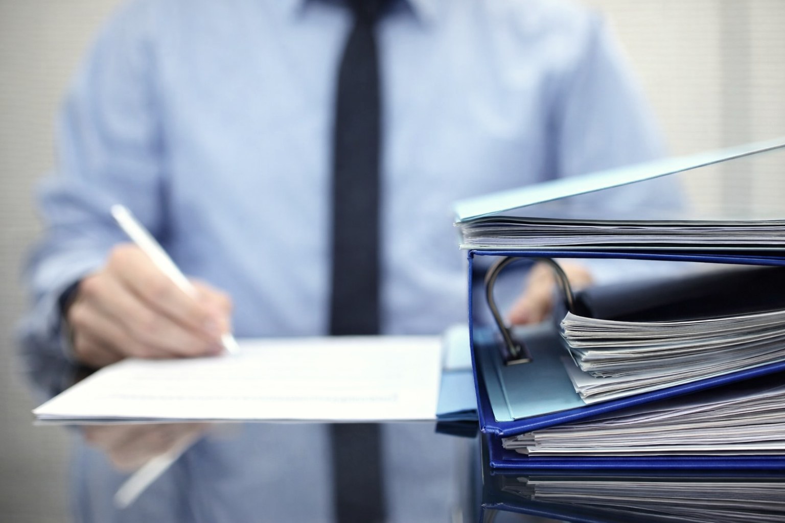 Stacks of unprocessed paperwork binders with a businessman in the background — the operational reality when tenement expenditure records fall behind